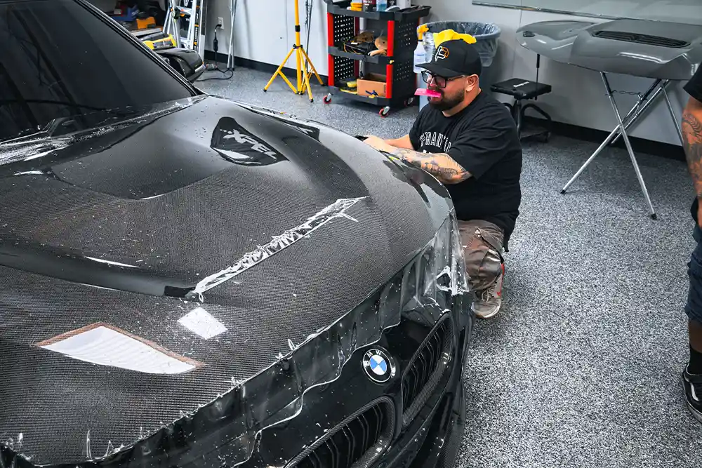 Xpel paint protection film being applied on a brand new carbon fiber BMW hood by Phantom Filmwerkz in Victorville California